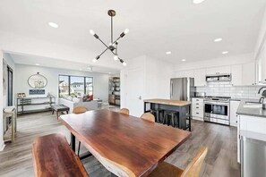 A modern kitchen with white cabinets, stainless steel appliances, and a wooden dining table. - Amazing home near beach, shopping & Ocean City - dog-friendly, central AC & W/D (Fenwick Island)