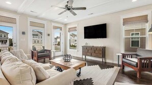 Ein geräumiges Wohnzimmer mit Sofa, Couchtisch und Sesseln, einem Deckenventilator und einem an der Wand befestigten Fernseher.