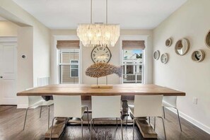 A dining room with a wooden table, white chairs, a chandelier, a wall clock, and decorative mirrors. - Resort Living in Bethany. AC/Pool and more. (Bethany Beach)