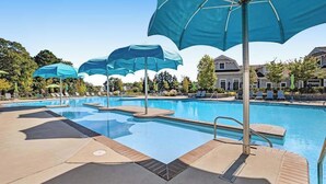 En swimmingpool med flera blå parasoller, solstolar och en klar himmel.