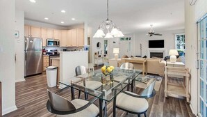 A modern kitchen with a refrigerator, microwave, and dining area with a glass table and chairs. - Bear Trap Dunes 1st floor condo w/ central AC, private W/D, and gas fireplace (Ocean View)