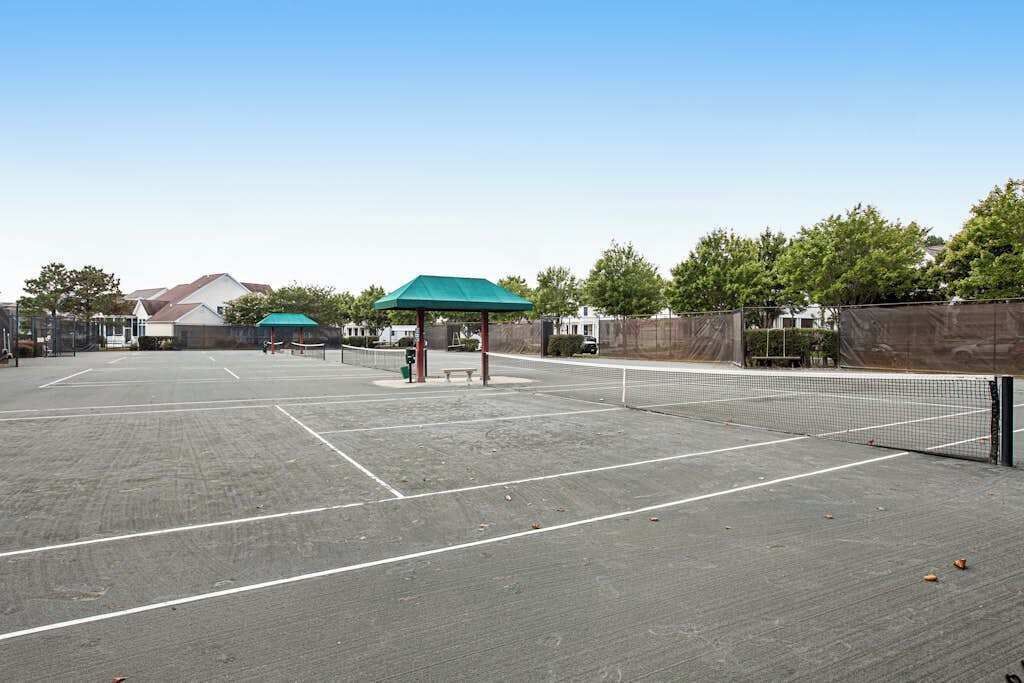 En udendørs tennisbane med net, en pavillon med grønt tag og et hegn.