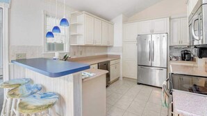 Una cocina moderna con armarios blancos, un refrigerador de acero inoxidable, una isla azul y taburetes de bar.