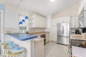 A modern kitchen with white cabinets, a stainless steel refrigerator, a blue island, and bar stools. - Clearwater - Jamestown Cir | House in Frankford (Frankford)
