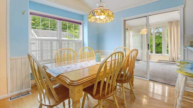 Comedor con una mesa de madera, seis sillas, una lámpara colgante de vitral y vistas al exterior a través de una ventana.
