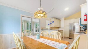 Un comedor con una mesa de madera, sillas, una lámpara colgante y una cocina con armarios y electrodomésticos.