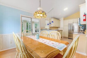 A dining area with a wooden table, chairs, a hanging light fixture, and a kitchen with cabinets and appliances. - Clearwater - Jamestown Cir | House in Frankford (Frankford)