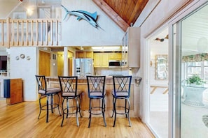 A modern kitchen with wooden flooring, a dining area with four chairs, and a large fish decoration on the wall. - South Bethany bay-view home with dock, deck, kayaks, & bikes (Bethany Beach)