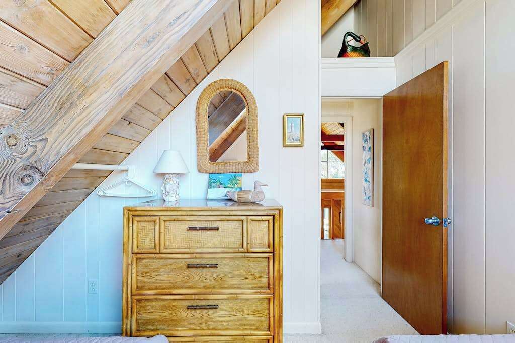 A room with a wooden ceiling, a wooden dresser with drawers, a mirror, and a door leading to another room.