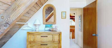 A room with a wooden ceiling, a wooden dresser with drawers, a mirror, and a door leading to another room.