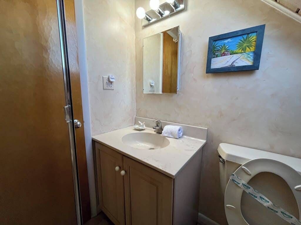 A bathroom with a sink, mirror, toilet, and a painting on the wall.