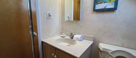 A bathroom with a sink, mirror, toilet, and a painting on the wall.