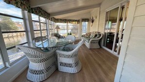 Una veranda coperta con mobili in vimini, ampie finestre e vista sull'acqua.