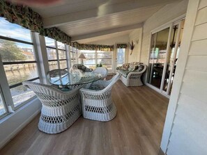 A covered patio with wicker furniture, large windows, and a view of the water. - South Bethany bay-view home with dock, deck, kayaks, & bikes (Bethany Beach)