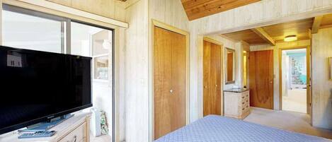 Un dormitorio con cama, televisión, paredes de madera, ventilador de techo y vista por la ventana.