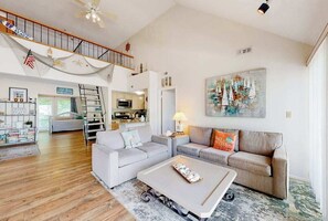 A spacious living room with a high ceiling, a staircase, a kitchen, and a dining area. - Sea Colony West - Waterfront condo with pool, beach access, tennis, & W/D (Bethany Beach)