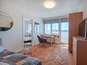 Ein modernes Zimmer mit einem Bett, einem Esstisch mit Stühlen, einem Fernseher und einem großen Fenster mit Blick.