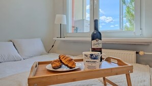 Un letto con biancheria bianca, un comodino con una bottiglia, una tazza e croissant su un vassoio.