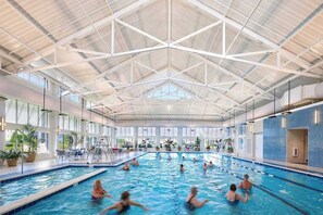 En indendørs swimmingpool med flere baner, højt til loftet med geometrisk design, og store vinduer der lukker naturligt lys ind.
