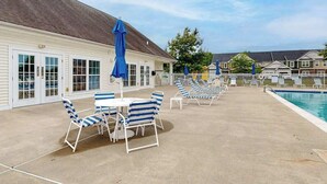 Ein Poolbereich mit Liegestühlen und Sonnenschirmen, einem Pool und einem Gebäude mit großen Fenstern.