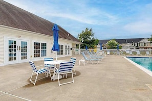 Ein Poolbereich mit Liegestühlen und Sonnenschirmen, einem Pool und einem Gebäude mit großen Fenstern.