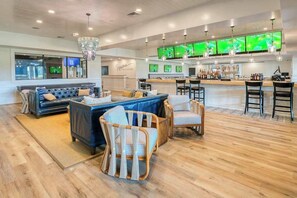 A modern bar area with multiple screens, a seating area with sofas and chairs, and a wooden floor. - Bayside Resort townhome with nautical-theme, resort amenities, & water views (Selbyville)