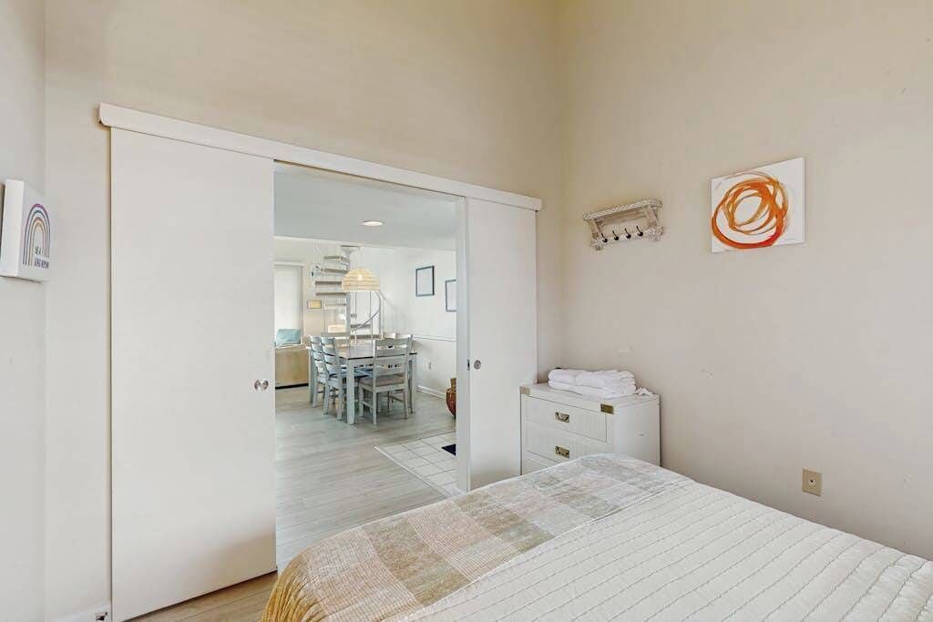 A bedroom with a bed, a dresser, a mirror, and a door leading to a dining area.
