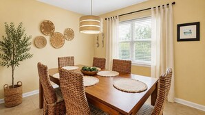 Un coin repas avec une table en bois, des chaises en osier, un luminaire suspendu et une plante en pot.