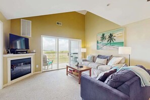 A living room with a television, a sofa, a coffee table, and a painting of a beach scene.