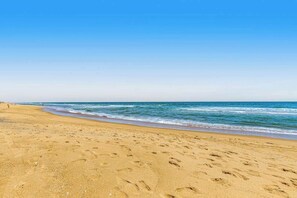 Ein sandiger Strand mit Fußabdrücken, die zum Wasser führen, ein klarer Himmel und eine ruhige See.