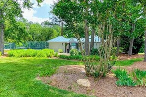A house with a green roof, surrounded by a well-maintained garden with various plants and a fenced area.