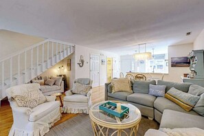 A living room with a staircase, a sofa set, a coffee table, and a dining area.
