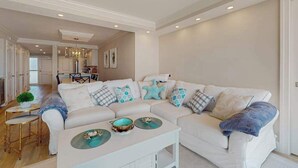 Una sala de estar con un sofá blanco, una mesa de centro y un comedor al fondo.