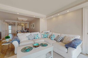 A living room with a white sofa, a coffee table, and a dining area in the background. - Sea Colony condo with balcony, pools, beach access, tennis & fitness centers (Bethany Beach)