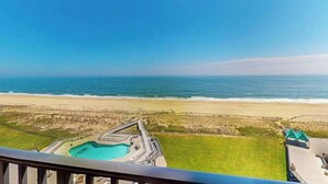 Vista a la playa desde un balcón con vista a una piscina y una playa de arena.