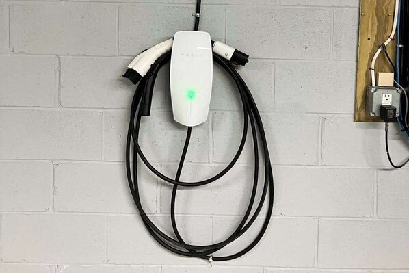 Pared blanca con una estación de carga de Tesla y un panel de madera con cableado eléctrico.