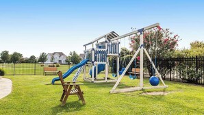 Un parque infantil con toboganes y columpios, rodeado por una valla y follaje.
