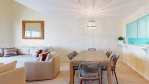 Un comedor con una mesa y sillas de madera, una lámpara de araña colgante, un sofá y un espejo en la pared.
