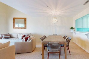 Ein Essbereich mit Holztisch und Stühlen, einer hängenden Chandelüstere, einer Couch und einem Spiegel an der Wand.