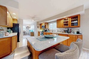A modern kitchen with wooden cabinets, a central island, and a seating area. - Spacious Salt Pond home with private deck & pool/hot tub/tennis access (Bethany Beach)