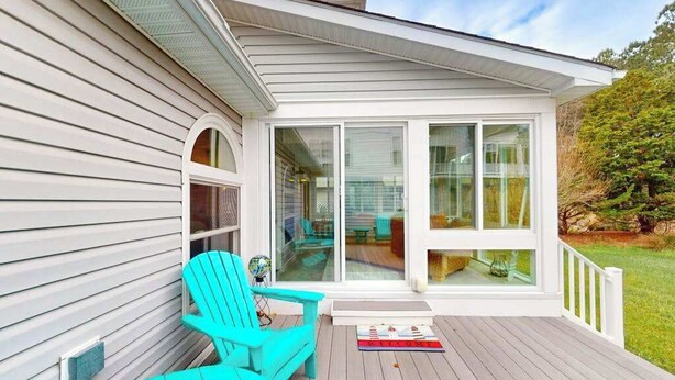 Eine überdachte Terrasse mit einer Schiebetür, einem türkisblauen Adirondack-Sessel und einem kleinen Teppich.