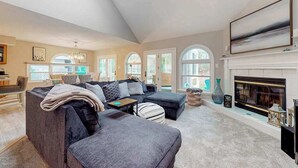 Ein geräumiges Wohnzimmer mit Kamin, großen Fenstern und einer modernen Deckenleuchte.