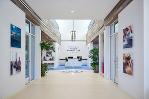 Eine moderne Lobby mit einer Rezeption, einem Schild mit der Aufschrift 'Welcome to the Health Aquatic Club' und einer Glaswand.