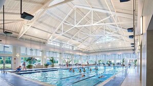 An indoor swimming pool with a high ceiling and large windows. - Bayside Resort home with bunk/playroom, deck, & access to pool, hot tub, & sauna (Selbyville)