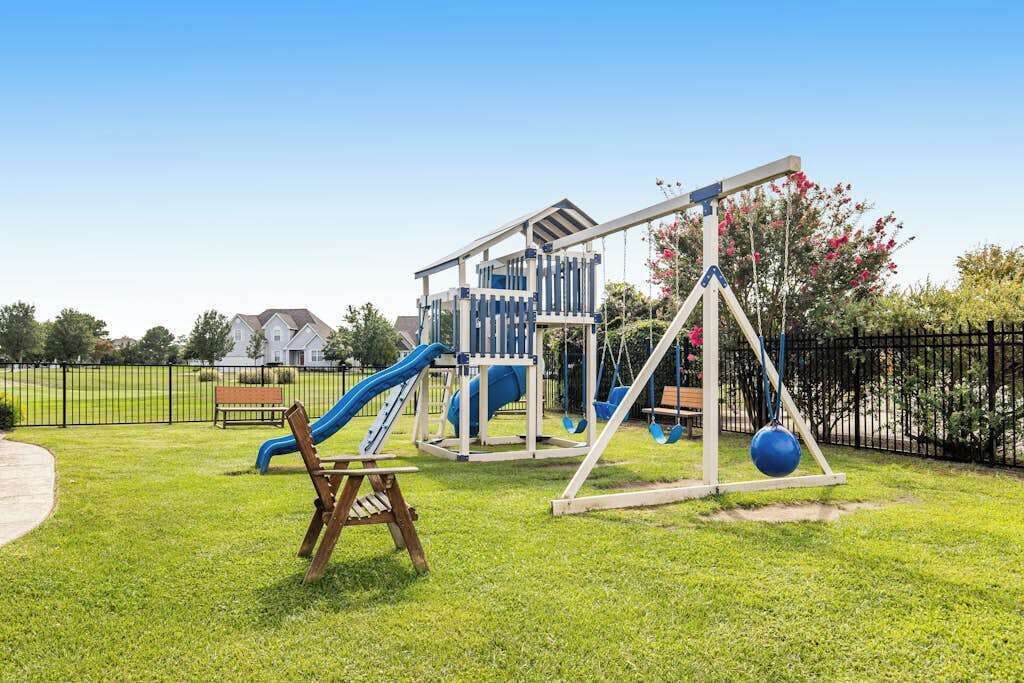 Un parque infantil con toboganes, columpios, un banco y una zona vallada.