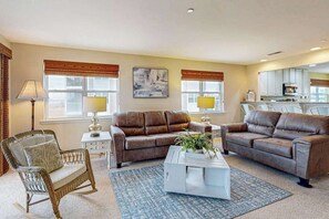 Ein Wohnzimmer mit zwei braunen Ledersofas, einem Korbstuhl, einem weißen Couchtisch und einem Gemälde an der Wand.