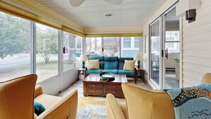 Una habitación con sofá, sillas, una mesa de centro y ventanas amplias.