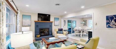 A living room with a fireplace, sofa, coffee table, and a dining area with chairs.