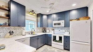 Una cocina moderna con armarios azul oscuro, electrodomésticos blancos y piso estampado.