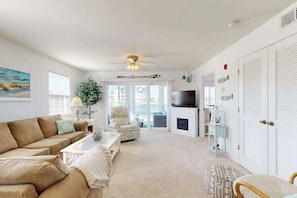 A living room with a sofa, coffee table, and a TV. There is a fireplace, a ceiling fan, and a view through a glass door. - 1st-floor Bethany Bay condo with bay views & on-site golf/pool/tennis (Ocean View)